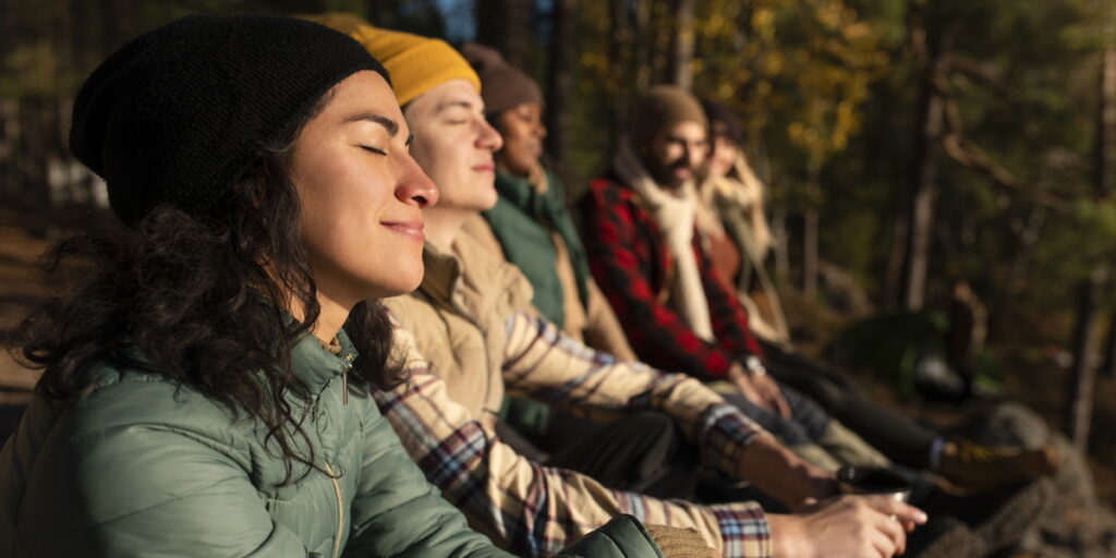 Side view of smiling woman with eyes closed enjoying sunlight while sitting by friends in forest.